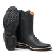 Bota de trabajo para hombre de piel graso color Negro con suela de hule, usada en ambiente de taller con jeans y guantes de trabajo. 