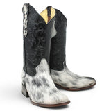 Bota vaquera para dama de pelo de vaca natural en tonos blanco y negro con punta cuadrada, tubo negro de piel con grabado cincelado floral y suela de cuero artesanal. Cada par presenta un patrón de pelo único. pair angle