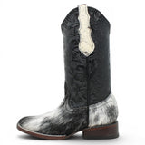 Bota vaquera para dama de pelo de vaca natural en tonos blanco y negro con punta cuadrada, tubo negro de piel con grabado cincelado floral y suela de cuero artesanal. Cada par presenta un patrón de pelo único.