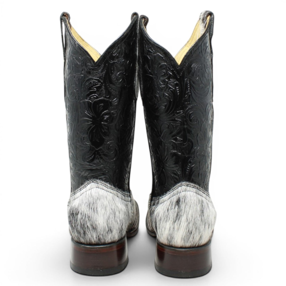 Bota vaquera para dama de pelo de vaca natural en tonos blanco y negro con punta cuadrada, tubo negro de piel con grabado cincelado floral y suela de cuero artesanal. Cada par presenta un patrón de pelo único. pair back
